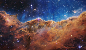 青い上部と、オレンジや茶色の起伏ある雲の境目に星々が点在する、ウェッブの「宇宙の崖」の観測画像。